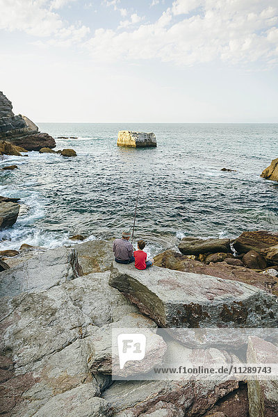 Grandfather and grandson fishing together at the sea sitting on rock