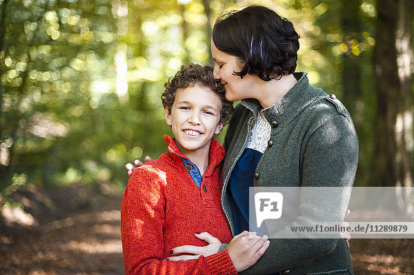 Portrait of smiling boy with his mother arm in arm in the autumnal forest