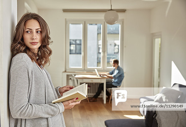 Woman with book leaning against wall at home