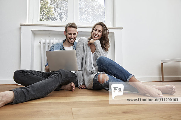 Smiling couple sitting on the floor with laptop