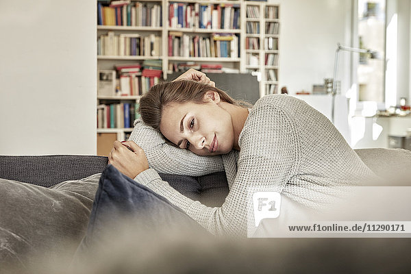 Tagträumende junge Frau entspannt auf der Couch im Wohnzimmer