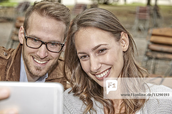 Porträt eines glücklichen Paares  das sich mit einem Smartphone im herbstlichen Biergarten vergnügt.