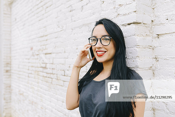 Smiling young woman on cell phone in front of brick wall