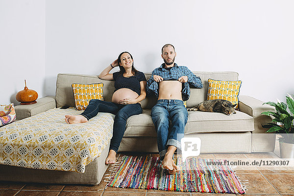 Happy couple expecting a baby sitting on couch at home with the cat
