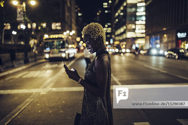 USA  New York City  lächelnde junge Frau am Times Square bei Nacht beim Blick aufs Handy