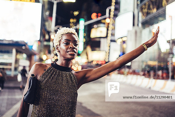 USA  New York City  junge Frau  die nachts am Times Square ein Taxi ruft.