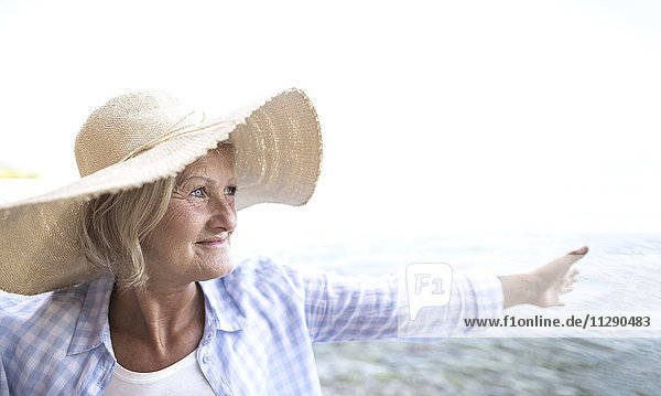 Glückliche reife Frau mit Strohhut am Strand