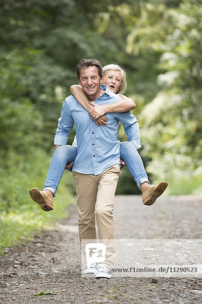 Smiling senior man giving his wife a piggyback ride on forest track