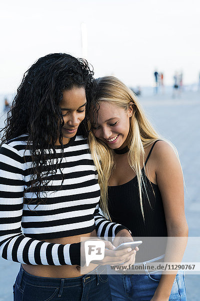 Zwei junge Frauen  die draußen auf ihr Handy schauen.