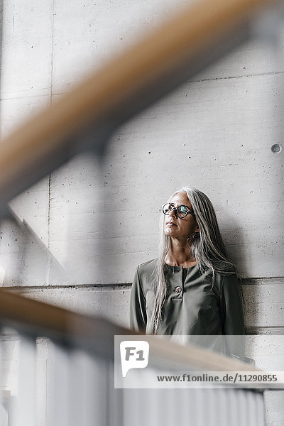 Woman with long grey hair leaning against a wall