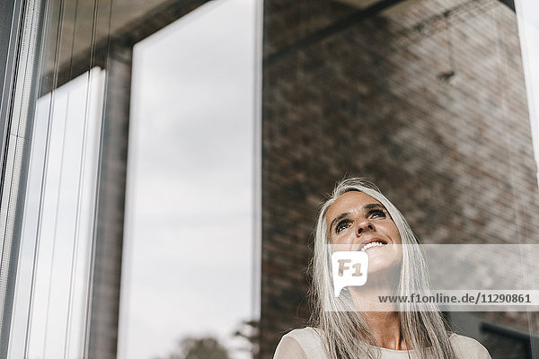 Smiling woman with long grey hair looking out of window