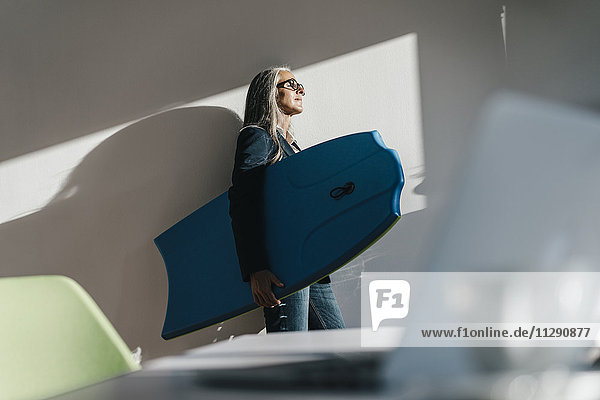 Geschäftsfrau im Büro hält Surboard und genießt Sonnenlicht