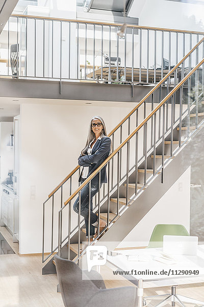 Smiling businesswoman with long grey hair standing on stairs
