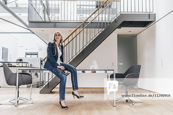 Businesswoman with long grey hair sitting on desk in office