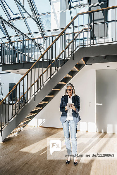 Businesswoman with long grey hair using tablet in a loft