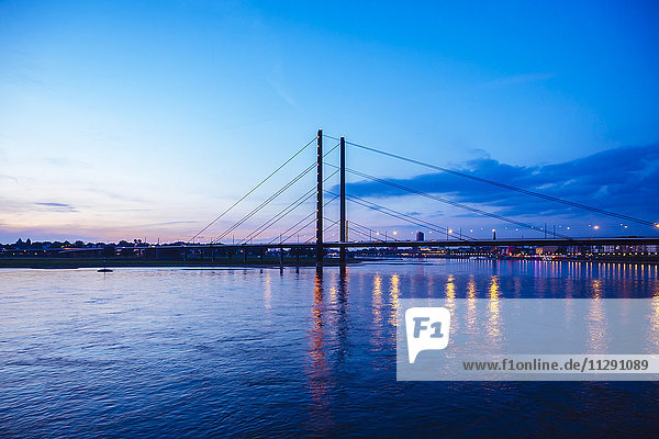 Deutschland  Düsseldorf  Blick auf Rheinknie-Brücke mit Rhein im Vordergrund zur blauen Stunde