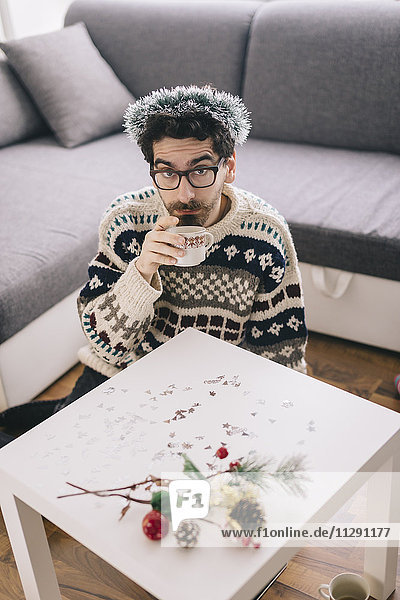 Einsamer junger Mann  der zu Hause zu Weihnachten Kaffee trinkt.