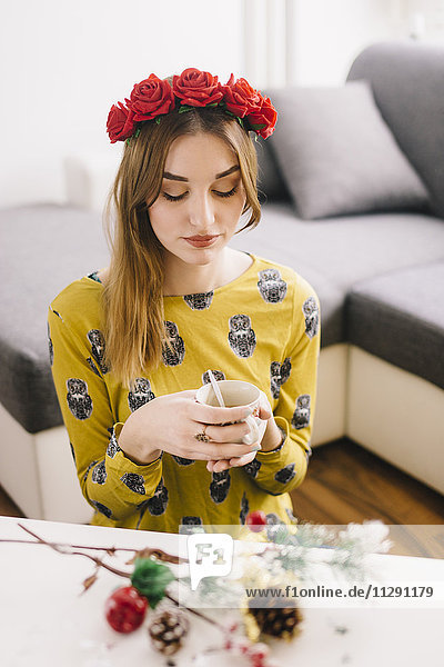Junge Frau mit Blumenkranz zum Entspannen bei einer Tasse Kaffee zu Hause zur Weihnachtszeit