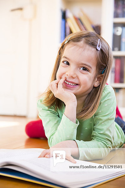 Portrait of smiling little girl lying on the floor with book