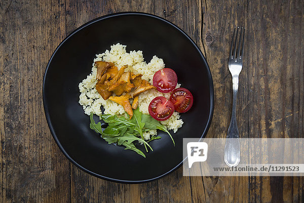 Schale mit Couscous-Salat mit Tomaten  Rucola und Pfifferlingen auf Holz