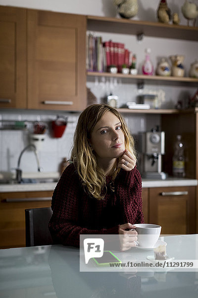 Porträt einer in der Küche sitzenden Frau mit einer Tasse Tee
