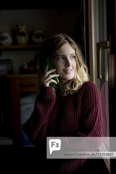 Porträt einer lächelnden Frau am Telefon mit Blick durchs Fenster