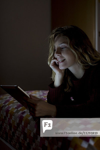 Frau liegt nachts auf dem Bett mit Tablette