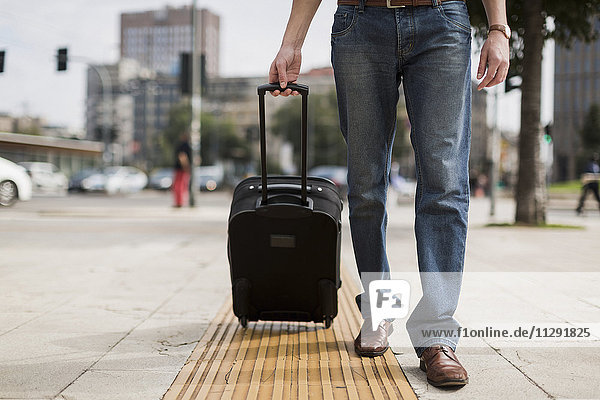 Beine des Geschäftsmannes mit Koffer auf dem Bürgersteig