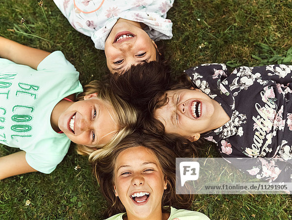 Vier lachende Mädchen liegen Kopf an Kopf auf einer Wiese.