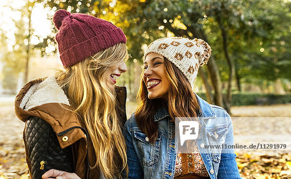 Zwei lächelnde junge Frauen mit Wollmützen in einem Park im Herbst