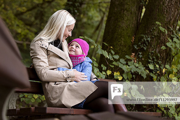 Mutter und kleine Tochter sitzen auf einer Bank im Herbstwald