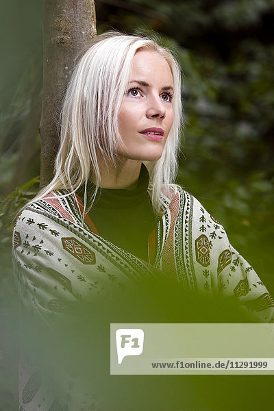 Porträt einer blonden Frau mit an den Baumstamm gelehntem Schal
