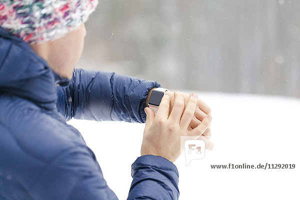 Sportlicher Mann beim Prüfen seiner Smartwatch im Winter