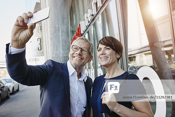 Businessman and businesswoman taking a selfie outdoors