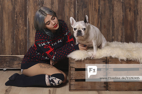 Junge Frau in Wintermode sitzend neben ihrer französischen Bulldogge