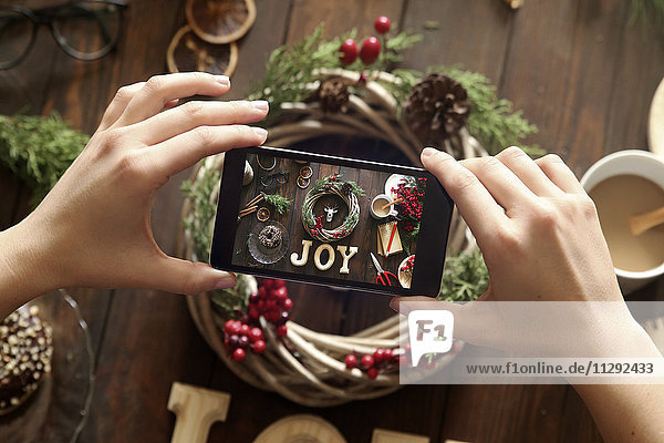 Frauenhände fotografieren selbstgemachten Adventskranz mit Smartphone