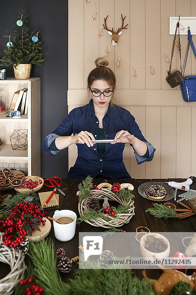 Frau fotografiert selbstgemachten Adventskranz mit Smartphone