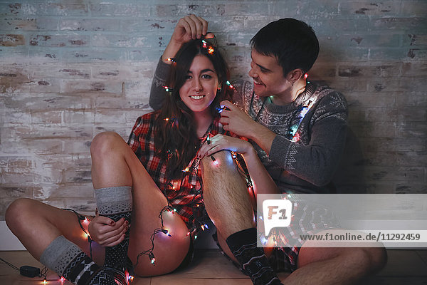Junges Paar auf dem Boden sitzend mit Lichterkette zur Weihnachtszeit