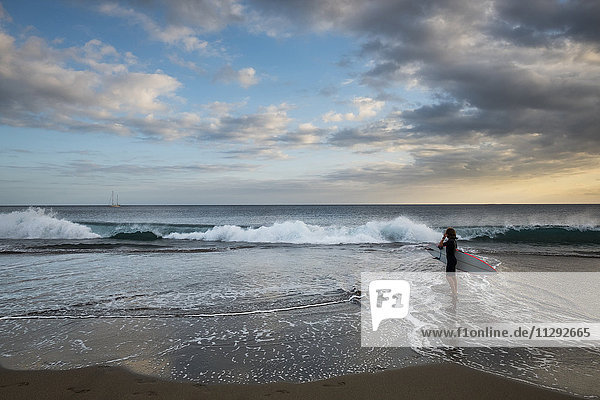 Spanien  Teneriffa  Junge mit Surfbrett am Strand bei Sonnenuntergang