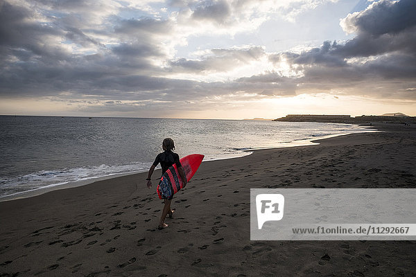 Spanien  Teneriffa  Junge mit Surfbrett am Strand bei Sonnenuntergang