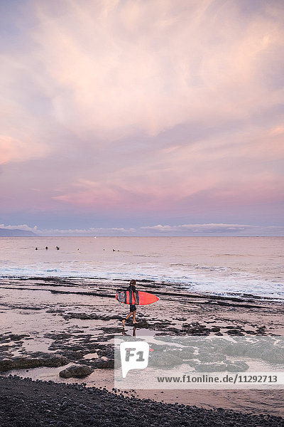 Spanien  Teneriffa  Junge mit Surfbrett am Strand bei Sonnenuntergang