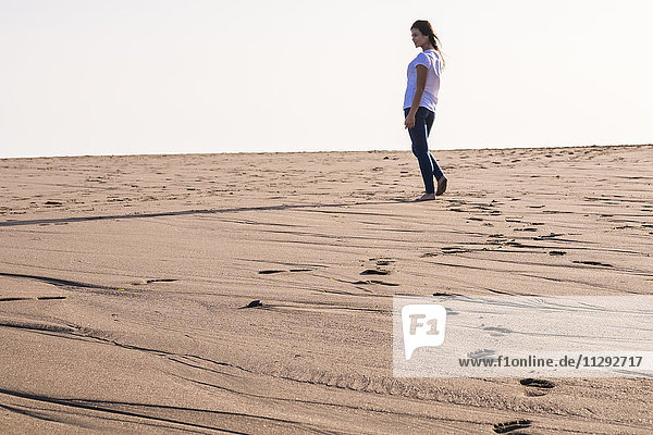 Junge Frau  die im Sand am Strand spazieren geht.
