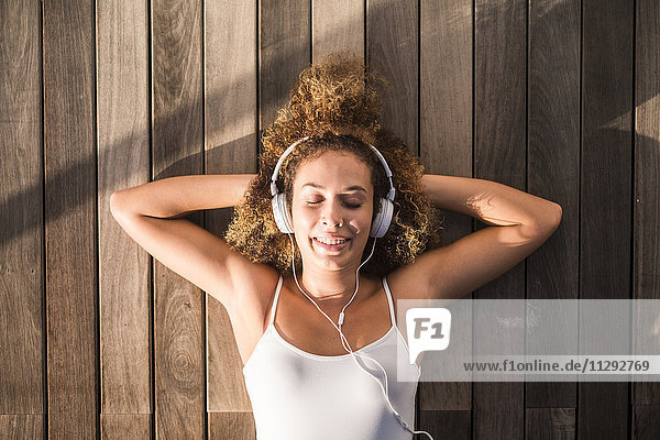 Porträt einer jungen Frau mit geschlossenen Augen auf Holzboden liegend  Musik hören mit Kopfhörer