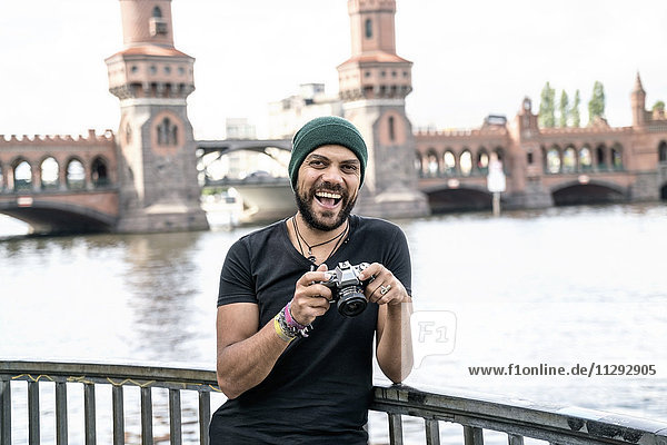 Deutschland  Berlin  Portrait des glücklichen Mannes mit Kamera vor der Oberbaumbrücke