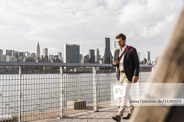 USA  New York City  Geschäftsmann  der am East River entlang läuft und sich das Handy ansieht.