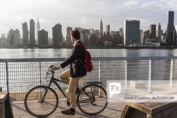 USA  New York City  Geschäftsmann auf dem Fahrrad mit Blick auf die Skyline von Manhattan