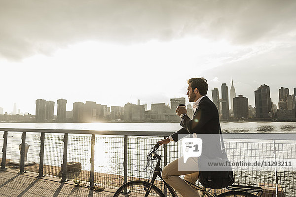 USA  New York City  Geschäftsmann auf dem Fahrrad mit Kaffee zum Mitnehmen