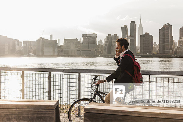 USA  New York City  Geschäftsmann auf dem Fahrrad im Gespräch mit dem Handy