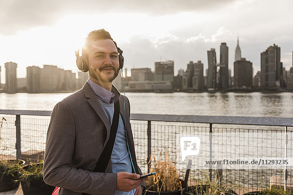 USA  New York City  Portrait eines lächelnden jungen Mannes mit Kopfhörer und Handy