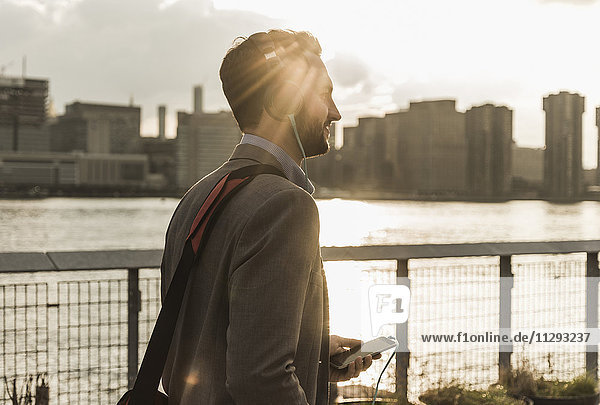 USA  New York City  junger Mann mit Kopfhörer und Handy am East River
